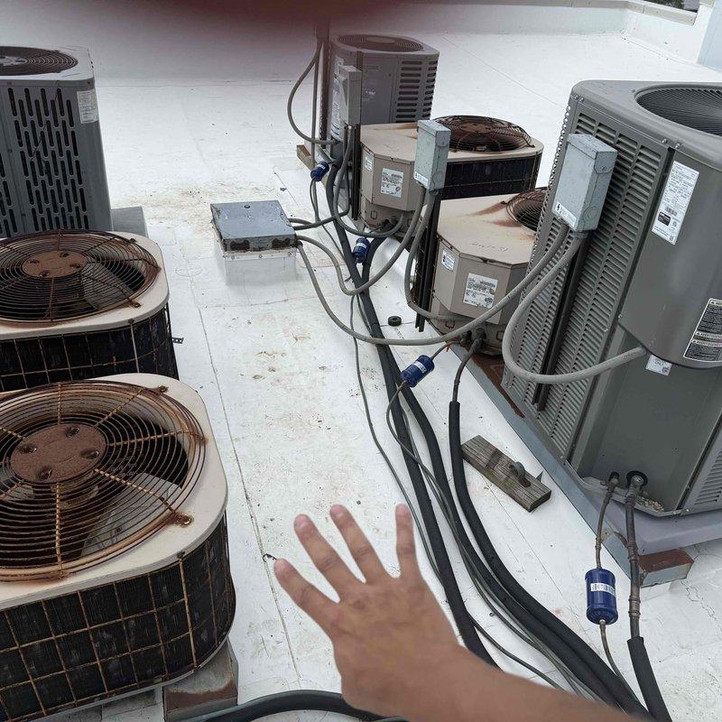 Conducted rooftop survey of commercial HVAC installation to identify air conditioning units operating without proper equipment pads. Inspected multiple condenser units of varying ages, including older cylindrical models and newer rectangular units, documenting equipment placement and support conditions. Photographed roof-mounted AC units, electrical disconnects, refrigerant line routing, and mounting configurations for assessment and future remediation planning.