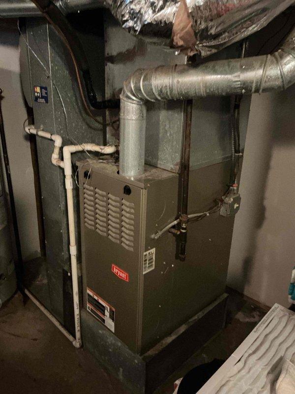 Responded to service call for air conditioning system not operating properly. Upon arrival, performed comprehensive diagnostic evaluation of split system including outdoor condensing unit and indoor air handler. Inspected outdoor unit positioned on concrete pad against building exterior, noting significant vegetation overgrowth around equipment that could potentially restrict airflow and reduce system efficiency. Examined refrigerant lines, electrical connections, and conduit routing along exterior wall. Assessed indoor furnace and air handling components in basement utility area, checking ductwork connections, electrical panel integration, and copper refrigerant piping. Documented equipment condition through photographs showing both outdoor condensing unit with cylindrical housing and mesh panel configuration, and indoor furnace with associated ductwork and utility connections. Completed system evaluation and provided customer with findings and recommended service options to restore p