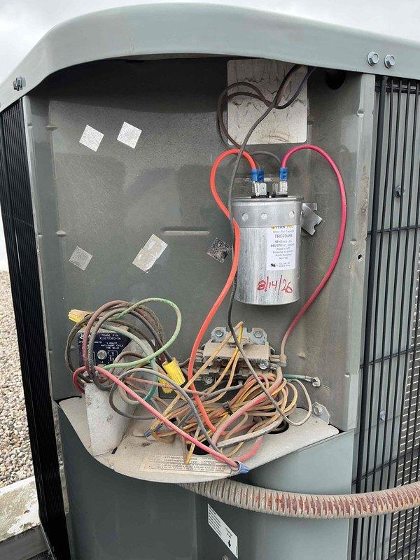 Responded to no cooling complaint on residential HVAC system with outdoor fan running but warm air discharge. Performed diagnostic inspection of outdoor condensing unit and verified thermostat settings, filter condition, and electrical supply. Upon accessing outdoor unit compartment, identified failed run capacitor as root cause of compressor failure to start. Capacitor showed visible signs of deterioration with date markings indicating age-related failure. Replaced defective dual run capacitor with manufacturer-approved replacement, restored proper electrical connections, and verified all wiring integrity. Cycled system through complete cooling operation, confirmed compressor engagement, proper amp draw, and cold air discharge at supply registers. System restored to full cooling capacity and normal operation.