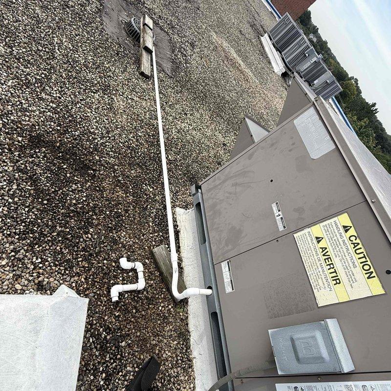 Repaired broken RTU condensate drain line by constructing new P-trap assembly and installing approximately 50-60 feet of PVC piping across rooftop to connect to existing drain point for adjacent RTU. Utilized various PVC fittings to properly route drainage system across gravel roof surface, ensuring proper pitch and secure connections throughout the installation.