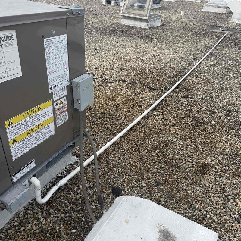 Repaired broken RTU condensate drain line by constructing new P-trap assembly and installing approximately 50-60 feet of PVC piping across rooftop to connect to existing drain point for adjacent RTU. Utilized various PVC fittings to properly route drainage system across gravel roof surface, ensuring proper pitch and secure connections throughout the installation.
