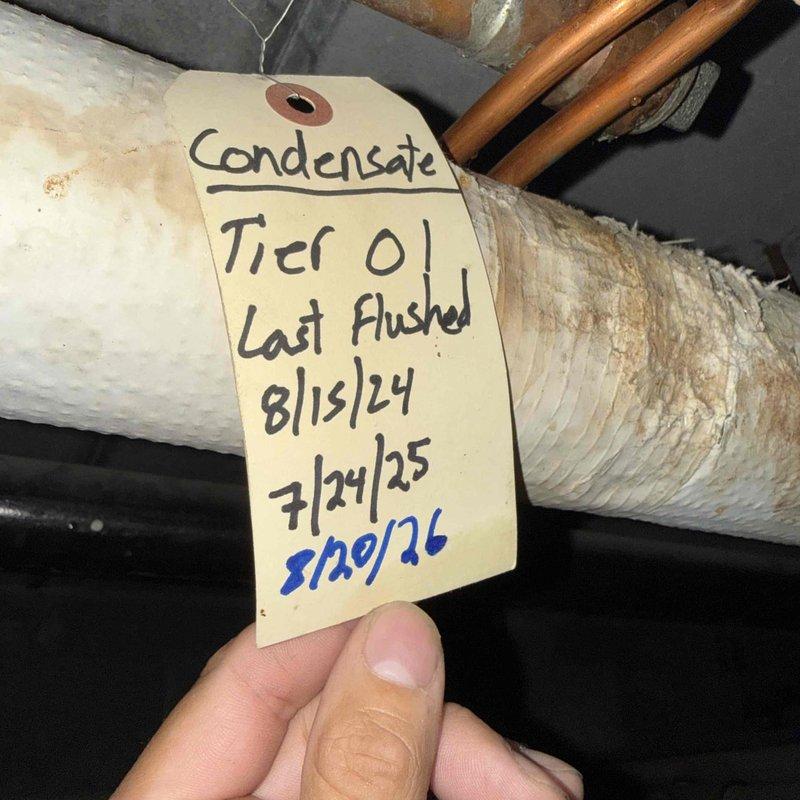 Responded to no cooling complaint at Unit 301 in multi-unit building. Upon arrival, discovered evidence of condensate drainage issue with water accumulation at exterior discharge point. Inspected building's common condensate drain system and located maintenance tag indicating last flush performed in August 2024. Confirmed condensate line blockage affecting building's shared drainage infrastructure. Coordinated with office to obtain building management approval for service work. Documented existing conditions with photographs showing saturated discharge area and condensate system components. Advised that issue originates from common building plumbing rather than individual unit equipment malfunction.