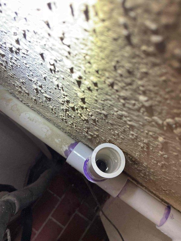 Responded to service call for water leak at furnace system. Upon inspection, identified leaking PVC condensate drain piping connected to furnace with compromised purple primer joints at T-fitting connection. Documented existing outdoor condensing unit condition and indoor furnace piping configuration. Assessed PVC drainage system for proper slope and connection integrity at T-junction fitting where active leak was occurring.