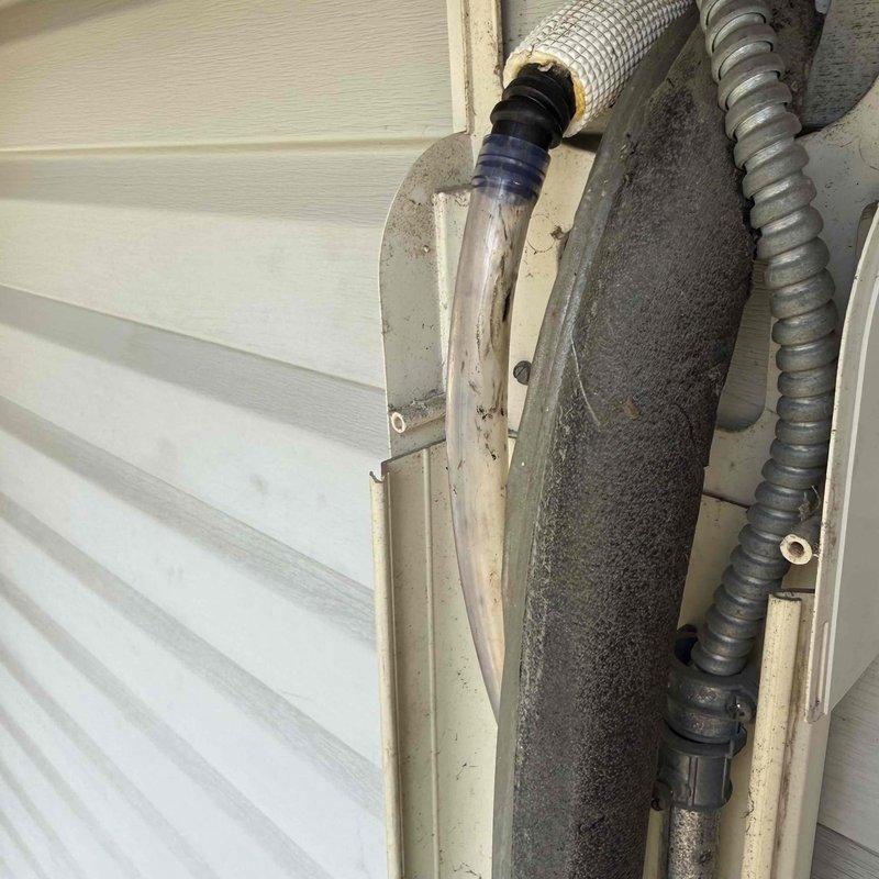 Responded to service call for ductless mini-split air conditioning system with reported severe water leakage. Upon arrival, performed diagnostic inspection of the indoor wall-mounted evaporator unit and exterior line set installation. Examined the refrigerant lines, condensate drainage system, and exterior conduit routing along building siding. Documented equipment condition and installation configuration with photographic evidence showing the line set penetration through exterior wall with protective covering and the indoor air handler unit mounted in corner location. Completed system evaluation to identify source of water leak and provided repair recommendations to resolve drainage issue.
