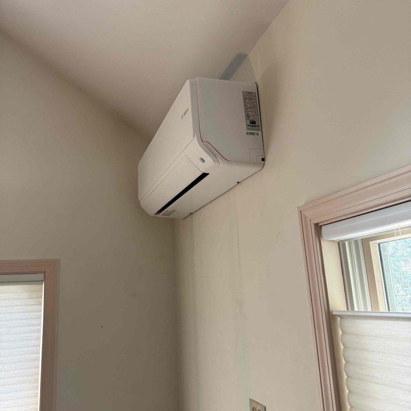 Responded to service call for ductless mini-split air conditioning system with reported severe water leakage. Upon arrival, performed diagnostic inspection of the indoor wall-mounted evaporator unit and exterior line set installation. Examined the refrigerant lines, condensate drainage system, and exterior conduit routing along building siding. Documented equipment condition and installation configuration with photographic evidence showing the line set penetration through exterior wall with protective covering and the indoor air handler unit mounted in corner location. Completed system evaluation to identify source of water leak and provided repair recommendations to resolve drainage issue.