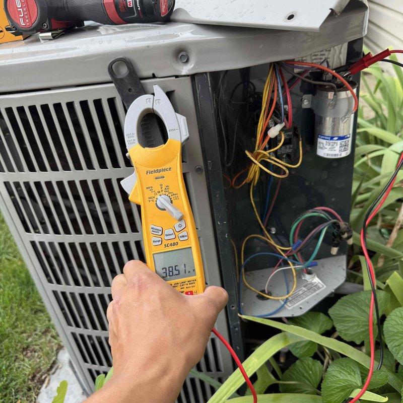 Responded to customer concern regarding lights dimming when air conditioning system operates. Performed diagnostic evaluation of outdoor condensing unit, measuring electrical draw with clamp meter which showed reading of 385.1 amps, indicating abnormally high amperage draw on startup. Inspected internal electrical components including capacitor, contactor, and wiring connections for potential issues causing excessive current demand that would affect household electrical system.