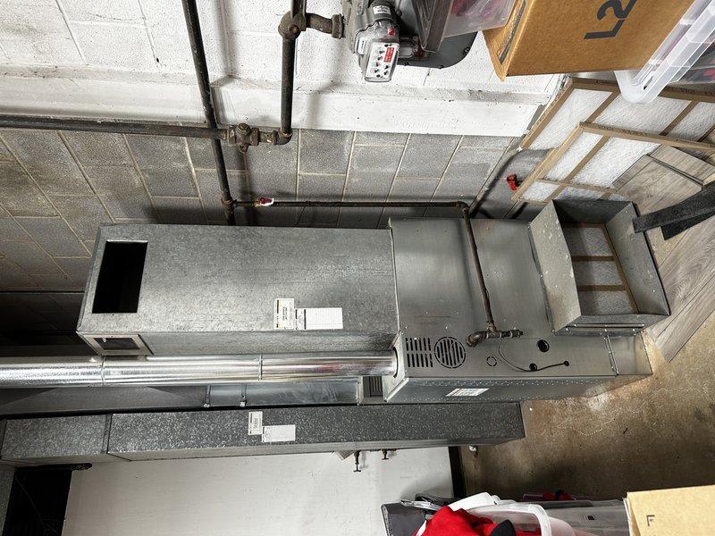 Performed field measurements of return air opening and ductwork on warehouse furnace system to provide accurate dimensions for commercial HVAC estimate. Documented return opening height at 13 inches and captured measurements of existing rectangular metal duct connections on the air handler unit. Photographed overhead HVAC installation including large rectangular sheet metal ductwork, air handler with blower compartment, and associated black piping connections mounted near drop ceiling for estimation and planning purposes.