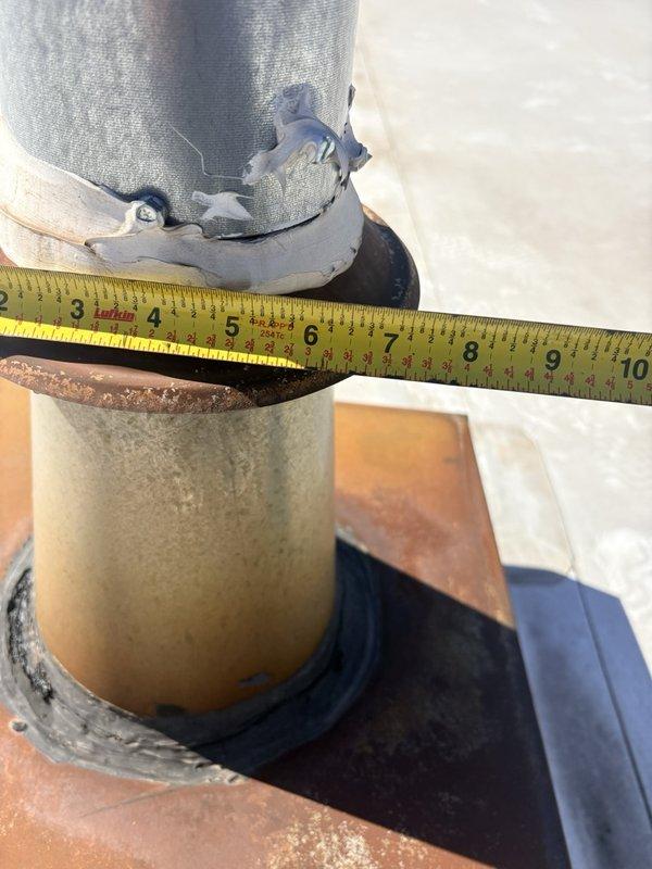 Responded to investigate water leak reported near flue penetration after roofer ruled out roofing system as source. Performed thorough inspection of roof-mounted vent pipe and flue assembly. Documented measurements of the cylindrical metal duct pipe, which measured approximately 7 inches in diameter. Found deteriorated insulation wrap at top of pipe with visible fraying and wear. Identified compromised rubber boot flashing at roof penetration point with signs of age-related deterioration. Discovered significant rust and corrosion on square mounting flange and curb adapter at base of pipe assembly, with brown and orange oxidation present around edges. Noted deteriorating tan-colored coating on flange and aging black rubber gasket seal where pipe meets flange. Determined that water intrusion was occurring at the flue penetration assembly due to failed weatherproofing components rather than roof membrane. Photographed all findings for documentation purposes. Recommended replacement of det