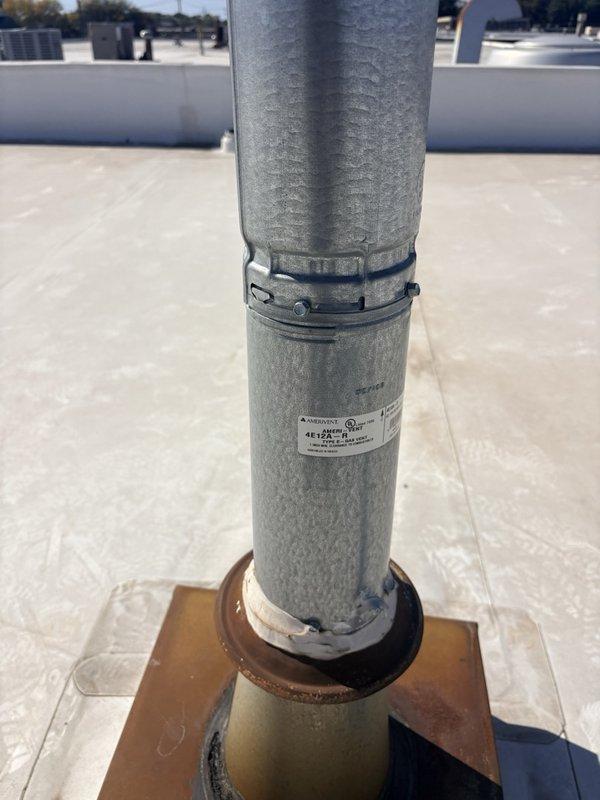 Responded to investigate water leak reported near flue penetration after roofer ruled out roofing system as source. Performed thorough inspection of roof-mounted vent pipe and flue assembly. Documented measurements of the cylindrical metal duct pipe, which measured approximately 7 inches in diameter. Found deteriorated insulation wrap at top of pipe with visible fraying and wear. Identified compromised rubber boot flashing at roof penetration point with signs of age-related deterioration. Discovered significant rust and corrosion on square mounting flange and curb adapter at base of pipe assembly, with brown and orange oxidation present around edges. Noted deteriorating tan-colored coating on flange and aging black rubber gasket seal where pipe meets flange. Determined that water intrusion was occurring at the flue penetration assembly due to failed weatherproofing components rather than roof membrane. Photographed all findings for documentation purposes. Recommended replacement of det