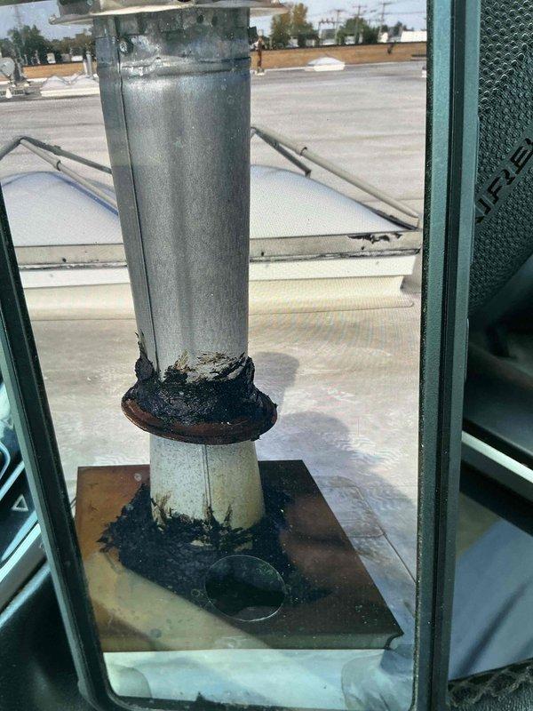 Removed deteriorated B-vent section from rooftop following recent furnace and coil replacement in warehouse. Installed rain cap on remaining vent pipe, applied roofing cement over rain collar and surrounding flat sheet metal base to seal cracked caulking and prevent water infiltration. Documented completed work with photographs showing proper sealing of vent termination assembly.