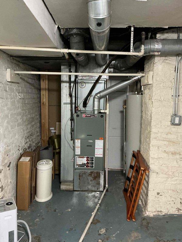 Responded to a no-cooling complaint and inspected the indoor Rheem gas furnace/air handler in the utility room, including the flue connection and cabinet condition, noting rust and discoloration at the base of the unit. Verified thermostat operation at the Honeywell Home ProSeries control, which was set to "Off" with the fan in the "On" position at a 77° indoor reading. Documented equipment information and system condition for service records.