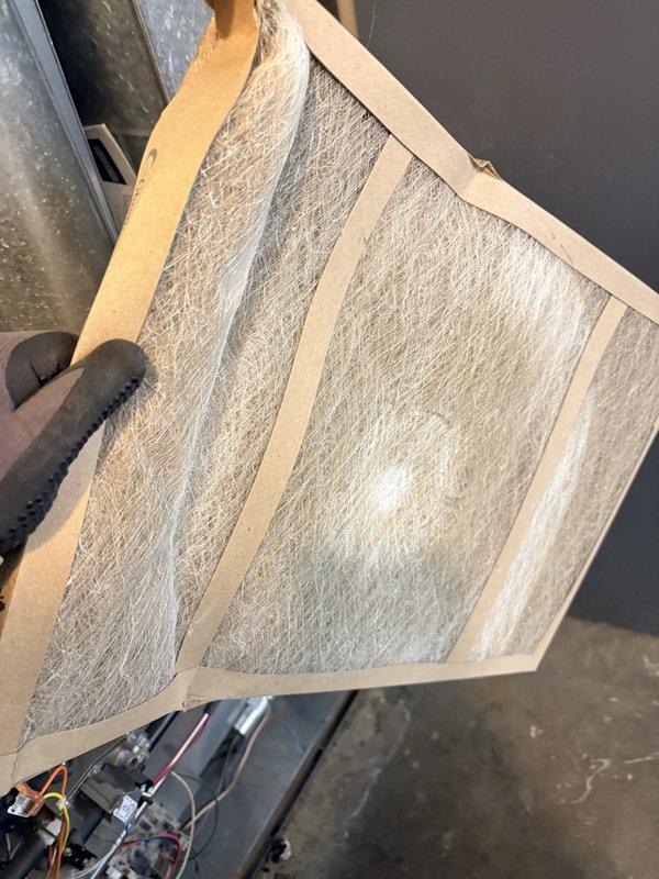 Performed a prepaid commercial maintenance visit on an upright gas furnace, inspecting the burner compartment, gas valve and manifold assembly, and associated wiring, and noting heavy dust and debris accumulation on the burner tubes and cabinet along with loosely routed control wiring. Inspected the fiberglass air filter, which showed dust loading, and documented the equipment data plate and filter information, with any required changes flagged for update to the filter list.