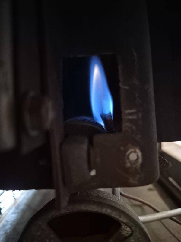 Relit the pilot on the gas space heater and confirmed ignition and stable burner operation, with a steady blue flame observed through the viewing port. Inspected the gas valve assembly and supply piping, noting heavy dust accumulation, surface corrosion on the iron elbow fitting, and deteriorated pipe coating, and recommended monitoring the connection and cleaning or servicing the unit to maintain safe, reliable operation.