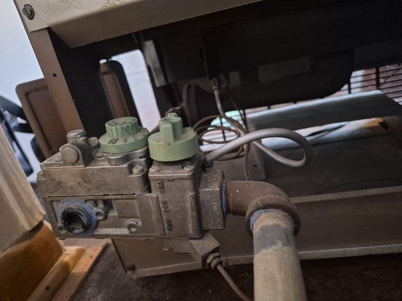 Relit the pilot on the gas space heater and confirmed ignition and stable burner operation, with a steady blue flame observed through the viewing port. Inspected the gas valve assembly and supply piping, noting heavy dust accumulation, surface corrosion on the iron elbow fitting, and deteriorated pipe coating, and recommended monitoring the connection and cleaning or servicing the unit to maintain safe, reliable operation.