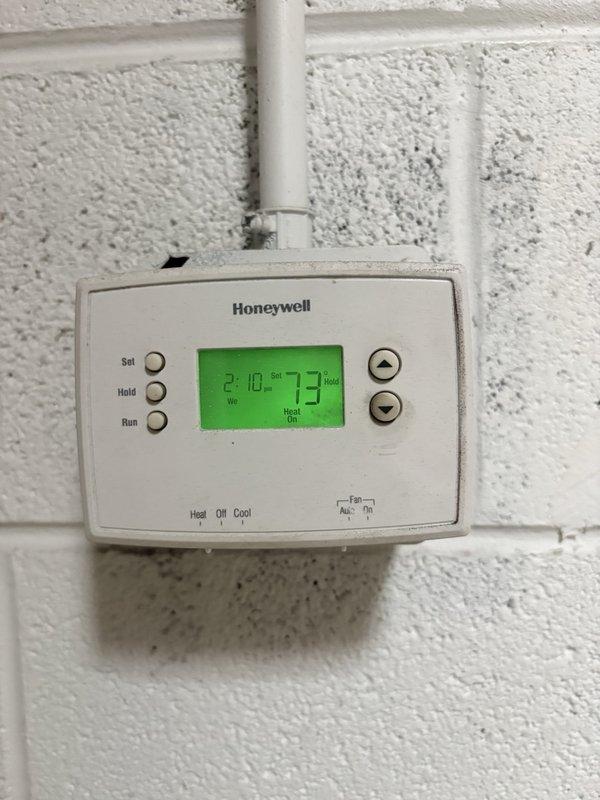 Performed scheduled preventive maintenance on a ceiling-suspended gas-fired unit heater, inspecting the cabinet, louvered grille, heat exchanger, motor and fan assembly, flexible gas connector, and black iron gas piping with shutoff valve; unit appeared intact with only minor surface dirt and light staining at the lower panel, and no frost or significant rust observed. Verified wall-mounted Honeywell thermostat operation in heat mode with a 73° setpoint and "Heat On" call displayed, noting dust and grime buildup on the thermostat housing. Documented equipment and filter information for the maintenance checklist; no filter list changes were identified.
