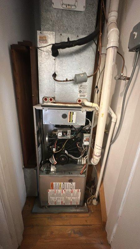 Performed diagnostic inspection on heating unit after tenant reported burnt smell. Examination of the furnace revealed exposed internal components including circuit board and wiring. Found water staining and deterioration around pipe installation area, which may be contributing to electrical issues causing the burnt odor. Recommended replacement of damaged components and sealing of water-compromised areas to prevent further damage.