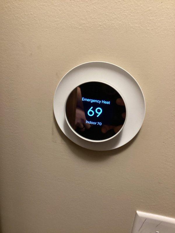 Responded to emergency heat call for older Carrier system. Inspected outdoor unit which was mounted on aging wooden platform with visible weathering. Found thermostat in emergency heat mode displaying 70° indoor temperature while set to 69°. Diagnosed failed heat pump operation causing system to rely on auxiliary heat. Restored primary heating function by replacing defective contactor and cleaning restricted condenser coil, restoring efficient operation.