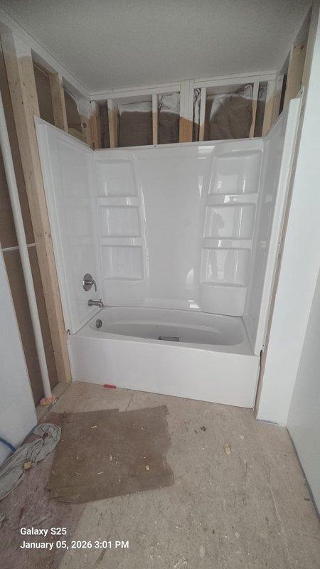 Completed rough-in installation of bathtub and shower unit with built-in shelving niches. Confirmed proper positioning of drain hardware and wall-mounted faucet/shower controls. Unit is now ready for final connections and fixture installation.