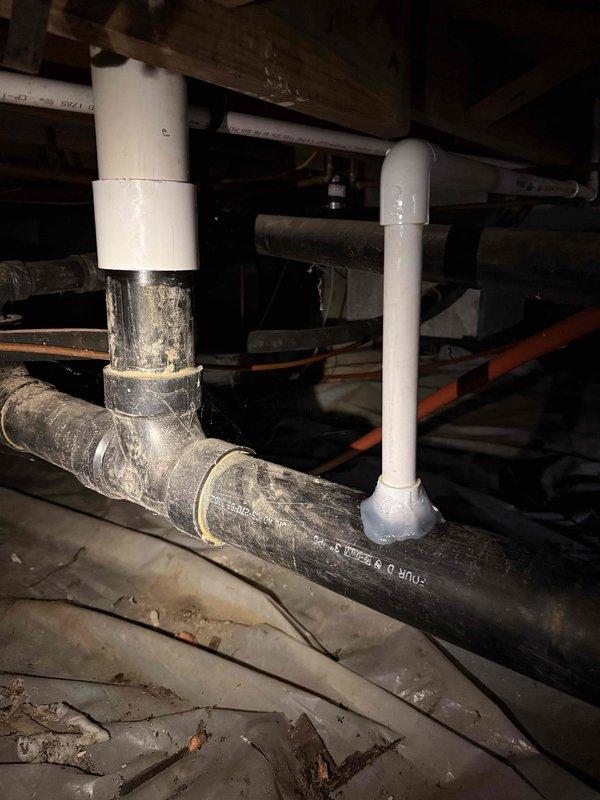 Inspected plumbing infrastructure in crawlspace to investigate gurgling sounds occurring during toilet flushes. Examined the connection between furnace drain pipe and sewer line, which was previously installed. Discovered the cause of the gurgling noise was related to the drain pipe configuration where the white PVC pipe connects to the black ABS drain pipes.