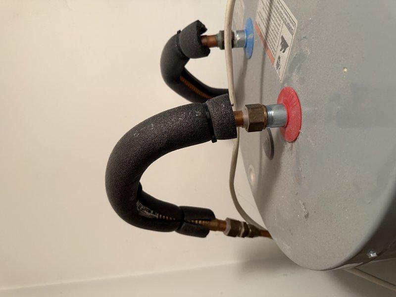 Responded to emergency service call for water heater leak reported by customer. Upon inspection, examined plumbing connections at water heater tank, focusing on hot and cold water line connections with their respective red and blue connector rings. Also inspected the electrical junction box and ventilation components. No active leaks were identified during inspection.