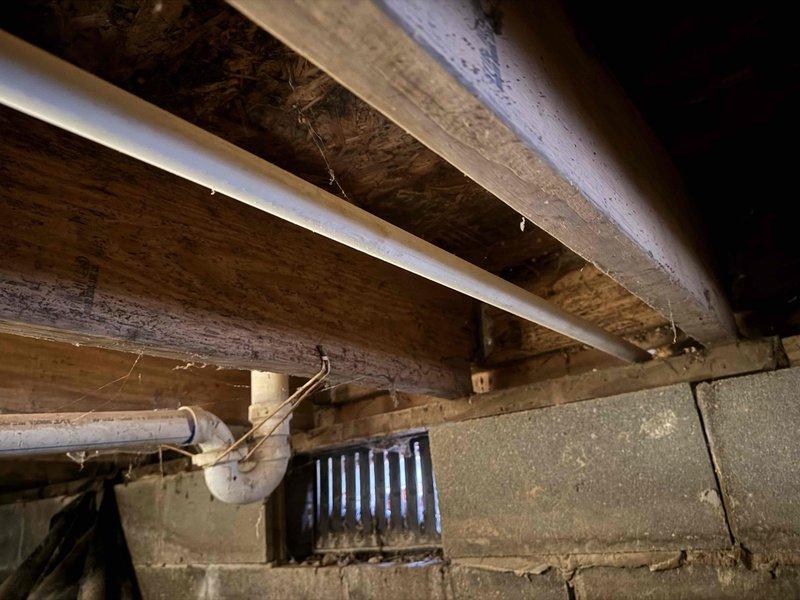 Technician returned to property to reroute condensate drain line to exterior of building as part of warranty service. Accessed crawlspace to modify existing PVC drainage system, ensuring proper installation through floor joists and connecting to exterior wall vent for appropriate condensate discharge.