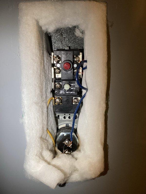 Responded to callback regarding water heater reset button repeatedly tripping. Inspected electrical components including thermostat control/relay switch and terminal connections. Accessed internal electrical control mechanism by removing cover panel and pulling back insulation. Examined wiring connections (red, yellow, blue, and black wires) to diagnose cause of thermal cutoff activation.