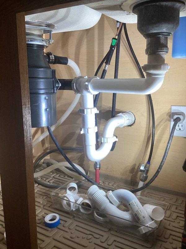 Responded to customer call regarding leak under kitchen sink. Diagnosed issue with faulty P-trap assembly. Removed existing white PVC drain components, replaced with new P-trap configuration, and verified proper connection to garbage disposal unit. System tested with no leaks observed after repair.