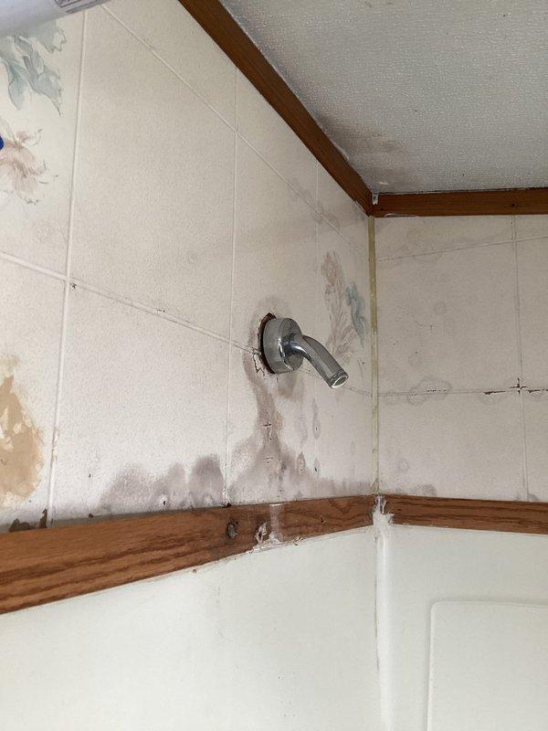 Responded to service call regarding lukewarm water heater repeatedly tripping breaker. Inspection revealed severely corroded anode rod requiring replacement and significant water damage around shower fixture with visible leakage staining surrounding tiles. Replaced anode rod and repaired leaking shower valve to prevent further water damage to wall structure.