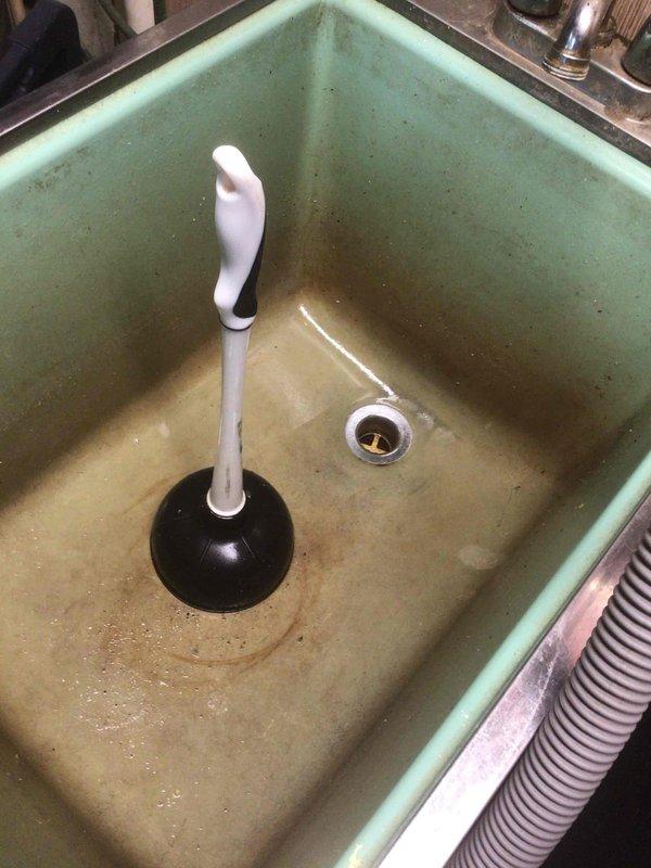 Cleared clogged utility sink drain where washing machine discharges. Addressed low water pressure issue in kitchen following pipe thawing event. Used plunger to remove obstruction in the mint green wash tub, restoring proper drainage functionality.