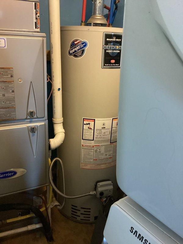 Conducted pre-inspection for bathroom renovation project involving replacement of existing tub and surround with new walk-in shower and glass doors. Examined wall cavity to assess plumbing infrastructure and photographed water heater system (Defender Safety System) with connected PVC piping to evaluate capacity and compatibility with planned installation.