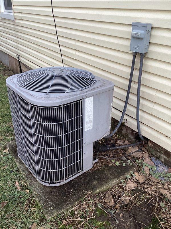 Performed diagnostic inspection of weathered outdoor AC condenser unit showing signs of environmental wear. Examined electrical connections at disconnect box and verified thermostat functionality, confirming proper operation with current temperature reading of 72°F and system set to "Heat On" mode with "Fan Auto" setting. Unit will require seasonal maintenance to address accumulated debris and weathering on exterior surfaces.