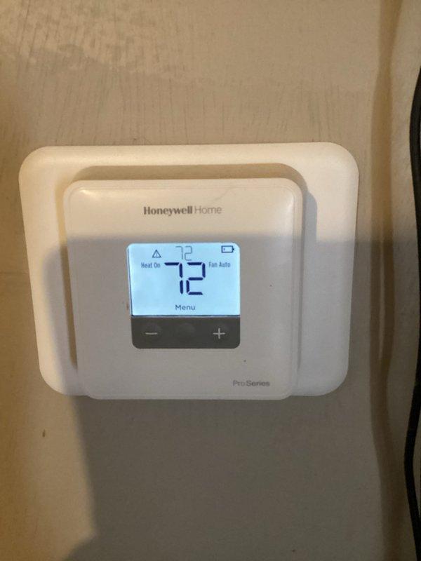 Performed diagnostic inspection of weathered outdoor AC condenser unit showing signs of environmental wear. Examined electrical connections at disconnect box and verified thermostat functionality, confirming proper operation with current temperature reading of 72°F and system set to "Heat On" mode with "Fan Auto" setting. Unit will require seasonal maintenance to address accumulated debris and weathering on exterior surfaces.