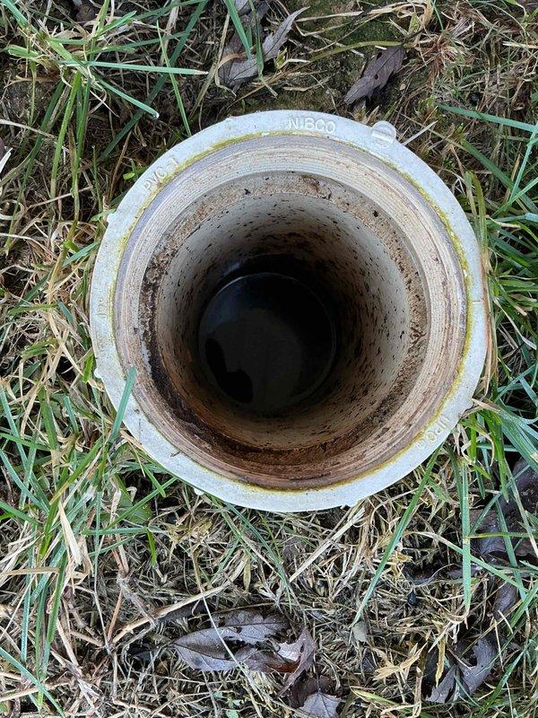Responded to service call for clogged exterior drain pipe. Upon inspection, found significant staining and sediment buildup in the cylindrical PVC drainage pipe located in the yard area. Cleared blockage and debris from drain opening, restoring proper drainage function.