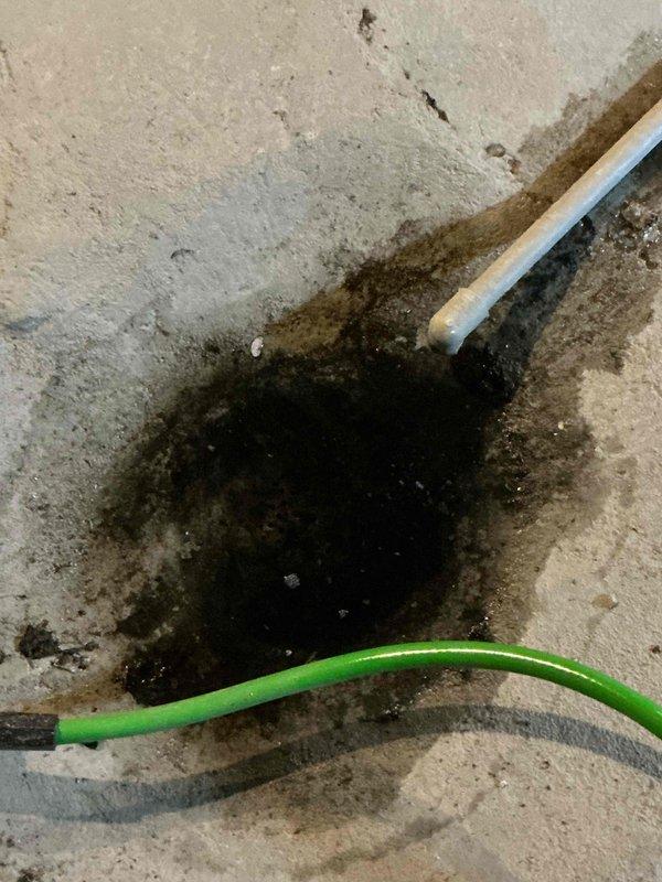 Inspected basement water intrusion affecting concrete flooring and wall joint. Identified significant moisture accumulation with visible water staining and potential mold development at the wall-floor intersection. Observed two exposed cables (white and green) running through the affected area which may contribute to safety concerns if water exposure continues.