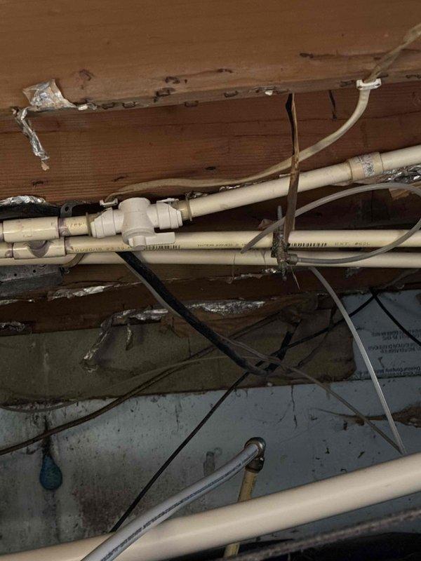 Conducted inspection of residential waterline issue, documenting exposed PVC piping system in crawlspace with visible joints and fittings. Observed signs of water damage and deterioration to surrounding wooden structural elements, with pipes mounted in disorganized manner beneath floor joists alongside various electrical wiring.