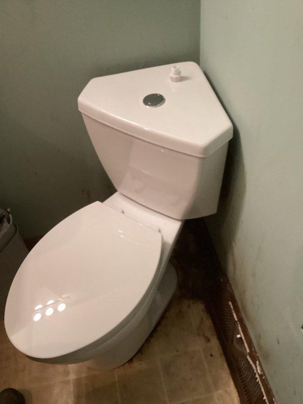 Successfully removed old corner toilet showing significant discoloration, mold growth, and floor staining, and replaced with new white triangular-tank corner toilet with top-mounted flush button. New installation properly set and sealed against both walls, optimizing space in the compact bathroom while resolving previous hygiene and potential water leakage issues.