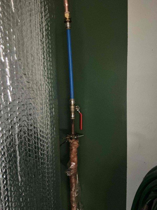 Completed prepaid plumbing maintenance inspection with focus on pipe assembly and toilet tank. Documented vertical pipe system with blue insulated section, copper connections, and red handle valve. Interior toilet tank inspection revealed aging components with mineral deposits, functioning fill valve with red cap, and standard mechanisms in working order.