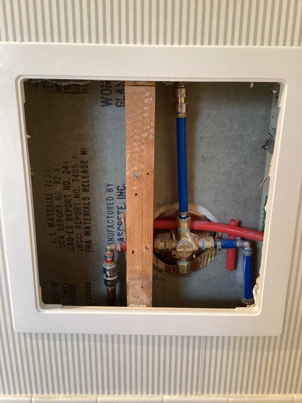 Removed and replaced shower valve, accessing plumbing through existing wall panel. Installed new brushed nickel handheld shower fixture with flexible hose and adjustable bracket. Confirmed proper water flow and functionality of new valve and showerhead assembly.