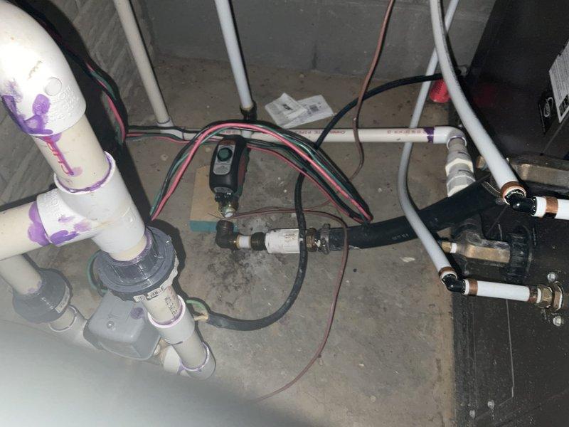 Conducted site assessment for potential conversion from open-loop geothermal system with well water supply issues to closed-loop configuration. Evaluated existing plumbing infrastructure in utility area, noting current PVC piping arrangement with pressure switch and control wiring. Surveyed available outdoor space for potential ground loop installation in cleared area adjacent to property.