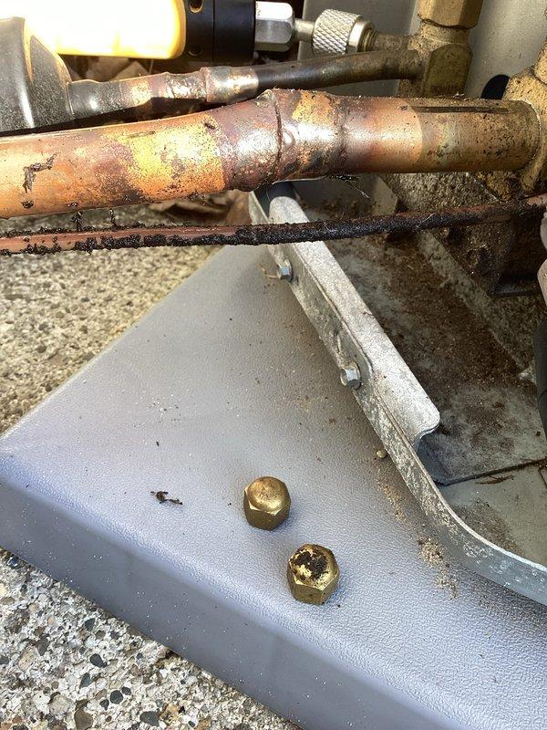 Responded to no-cooling complaint on residential air conditioning system. Inspection revealed significant corrosion and oxidation on refrigerant lines at the outdoor condensing unit. Determined system has developed a refrigerant leak at the copper piping connection, causing insufficient cooling capacity despite fan operation. Photographed damaged components for documentation.