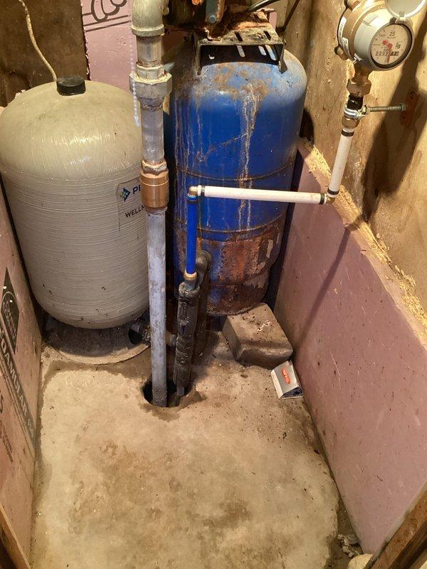 Conducted free estimate for connecting new city water service from municipal water pit to residence. Observed existing water entry point with deteriorated concrete penetration housing both PVC and black pipes. Noted significant corrosion on blue pressure tank with extensive rust formation, paired with white auxiliary tank in basement utility area. System includes visible water meter and requires complete service line replacement with proper sealing at foundation penetration point.