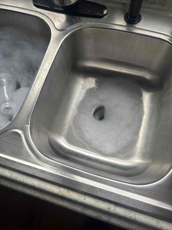 Successfully cleared clogged drain in commercial kitchen double-basin sink that showed significant mineral buildup and residue around drain area. Also inspected bathroom toilet for proper functioning as part of comprehensive plumbing service.