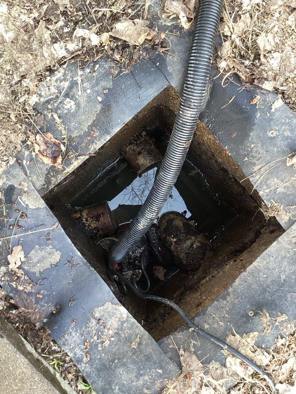 Inspected outdoor waste pump system, finding standing water in access pit with partially submerged plumbing components. Identified corrugated drainage pipe installation across lawn with visible soil disturbance, suggesting recent maintenance. Conducted evaluation of connector box and surrounding pipe infrastructure for maintenance planning.