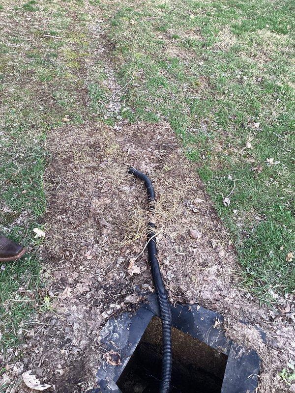 Inspected outdoor waste pump system, finding standing water in access pit with partially submerged plumbing components. Identified corrugated drainage pipe installation across lawn with visible soil disturbance, suggesting recent maintenance. Conducted evaluation of connector box and surrounding pipe infrastructure for maintenance planning.