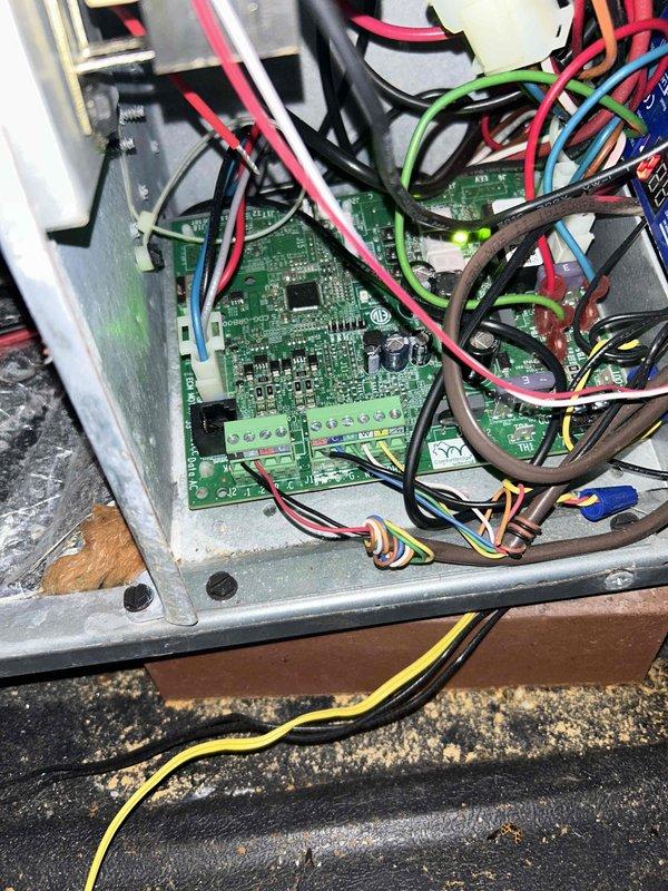 Performed diagnostic assessment of non-functioning heat pump system located in attic space. Inspected internal control board circuitry and connections, noting multiple colored wires (red, black, green, blue, yellow, brown, white) connected to the main circuit board. System was displaying error code and failing to initiate heating cycle; documented condition with photographic evidence of control panel interior and unit installation environment.