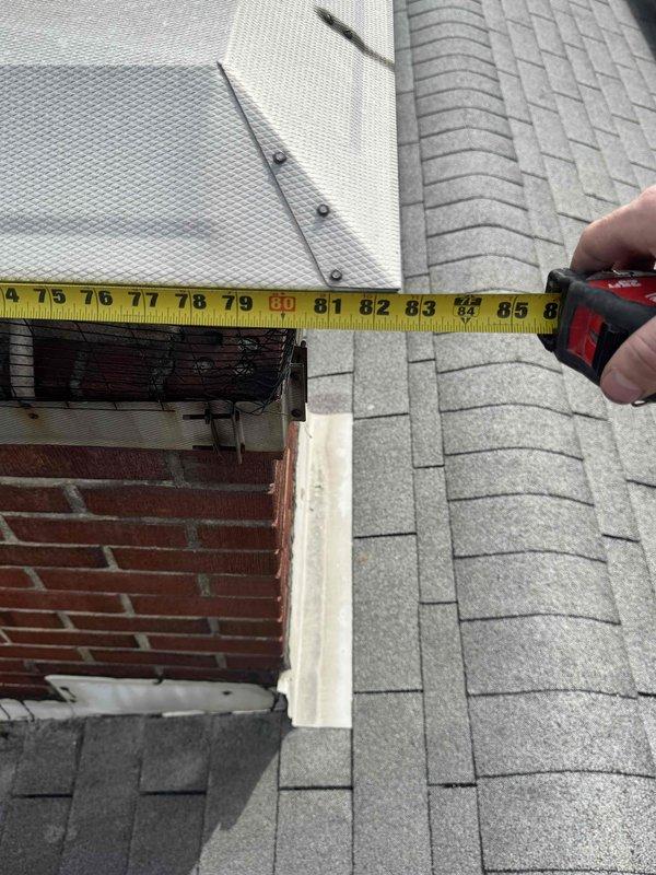 Conducted warranty inspection of flue installation, taking measurements of the brick chimney structure and surrounding roof area. Documented dimensions of approximately 85 inches across the roof section and 17-34 inches at the chimney, verifying proper clearances and installation specifications to address reported flue issues.