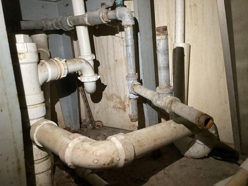# Plumbing Estimate - Complete System Replacement

Responded to service call regarding comprehensive plumbing system evaluation for potential full replacement. Customer reported uncertainty about current system functionality and condition of existing fixtures. Performed thorough assessment of accessible plumbing infrastructure throughout property.

Inspected bathroom fixtures including wall-mounted tank toilet with exposed internal mechanisms. Tank lid was removed during evaluation to assess flush valve, fill valve, and flapper condition. Noted split-seat configuration and overall fixture age consistent with older installation. Examined floor-mounted toilet bowl connection and checked for signs of leaking, deterioration, or structural concerns around base mounting area.

Conducted detailed inspection of exposed PVC drainage and supply piping system in utility area. Documented extensive network of white PVC pipes with multiple 90-degree elbows, horizontal and vertical runs, and various 