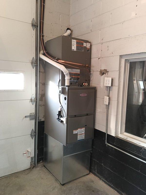 Completed full HVAC system installation in utility room consisting of Lennox furnace with air handler mounted vertically on concrete block wall. Installed copper refrigerant lines with insulation running between units, connected spiral ductwork to upper plenum, and routed all piping along wall for clean professional appearance. System fully operational with all components properly mounted, electrical connections completed, and equipment tested for proper function.