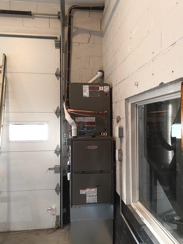 Completed full HVAC system installation in utility room consisting of Lennox furnace with air handler mounted vertically on concrete block wall. Installed copper refrigerant lines with insulation running between units, connected spiral ductwork to upper plenum, and routed all piping along wall for clean professional appearance. System fully operational with all components properly mounted, electrical connections completed, and equipment tested for proper function.