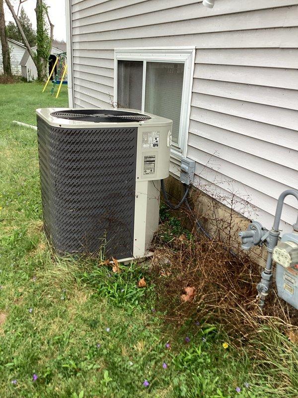 # HVAC Service Call - No Cooling Issue

Responded to no cooling complaint on residential air conditioning system over 10 years old. Upon arrival, verified Honeywell Home Pro Series thermostat was calling for cooling with display reading 73°F. Proceeded to outdoor unit located on concrete pad against house exterior. Found cylindrical condenser unit with black mesh protective grille heavily surrounded by yard debris, dead plant material, pine needles, and twigs accumulated around base and blocking airflow at ground level.

Cleared all debris from around unit perimeter and removed organic material restricting air intake. Inspected electrical disconnect and conduit connections - found secure with no visible damage. Cleaned condenser coil fins of dirt and vegetation buildup to restore proper heat exchange. Verified unit startup, checked amperage draw on compressor and fan motor - readings within manufacturer specifications. System now cooling properly with adequate airflow restored. Recomme
